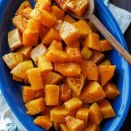 Roasted butternut squash on a blue oval platter with a serving spoon.