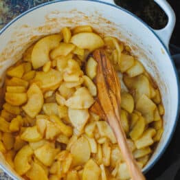 Sauteed cinnamon apples in a large pot with a wooden spoon.