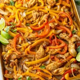 sheet pan chicken fajitas cooked on a cookie sheet with chicken, red and yellow peppers, onions and lime wedges