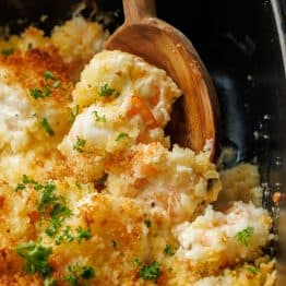 Wooden spoon scooping shrimp casserole out of a dish
