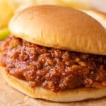 Sloppy Joe up close with saucy sloppy joe filling on a bun served with pickles and chips