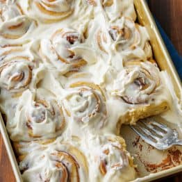 Sourdough cinnamon rolls frosted in a baking pan with 1 cinnamon roll removed