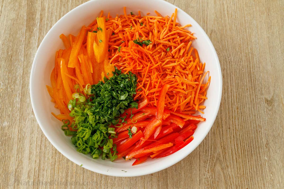 Shredded vegetables in a white bowl including peppers and herbs