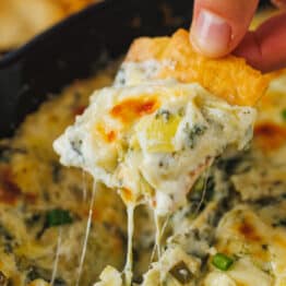 Cheesy spinach and artichoke dip scooped onto a chip with cheese pulls