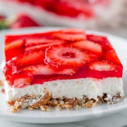 A slice of Strawberry Pretzel Salad on a white plate with the whole dessert in the background