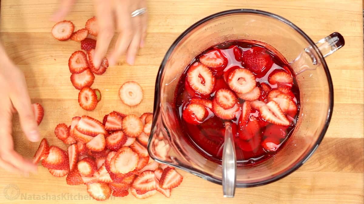 Sliced strawberries added to a measuring cup of liquid jello