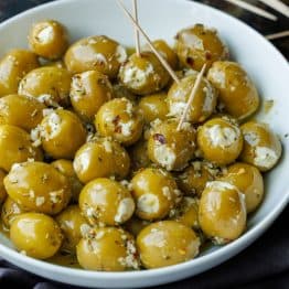 Stuffed green olives with white Boursin cheese, in a white bowl. Some olives have toothpicks for serving.