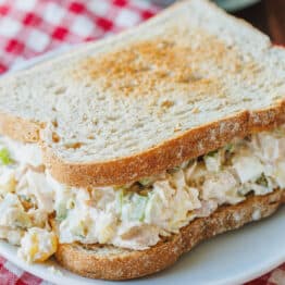 A classic tuna salad sandwich on a white plate, with a red and white checked cloth underneath.
