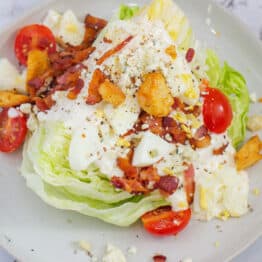 Wedge salad served on a plate with dressing and toppings